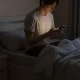 فردی در اتاق خواب با نور ملایم گوشی؛ تصویر پناهگاه صفحه نمایش و تعویق اندیشیدن در زندگی روزمره